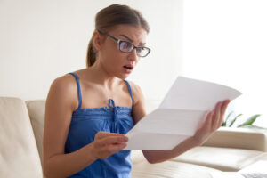 attractive young woman in eyeglasses feeling shocked because of written notice from bank